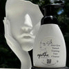Bottle of apothe Silk Aloe Glow Natural Foaming Face Cleanser on a mannequin head with blurred greenery in the background