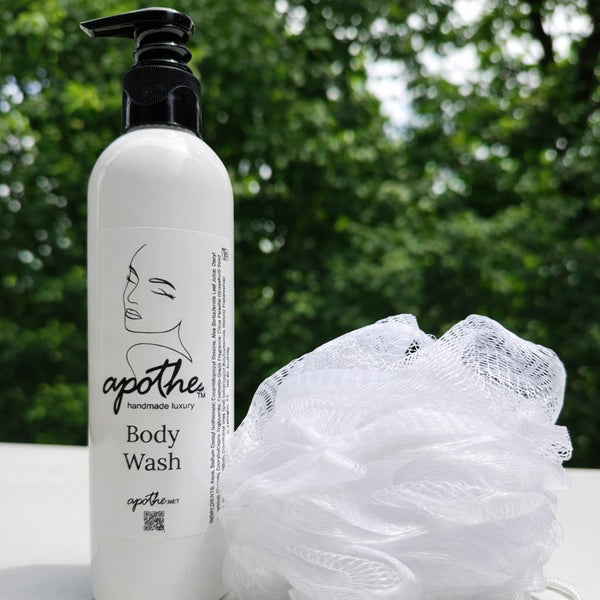 Body wash bottle with a loofah on a white surface with a green blurred background