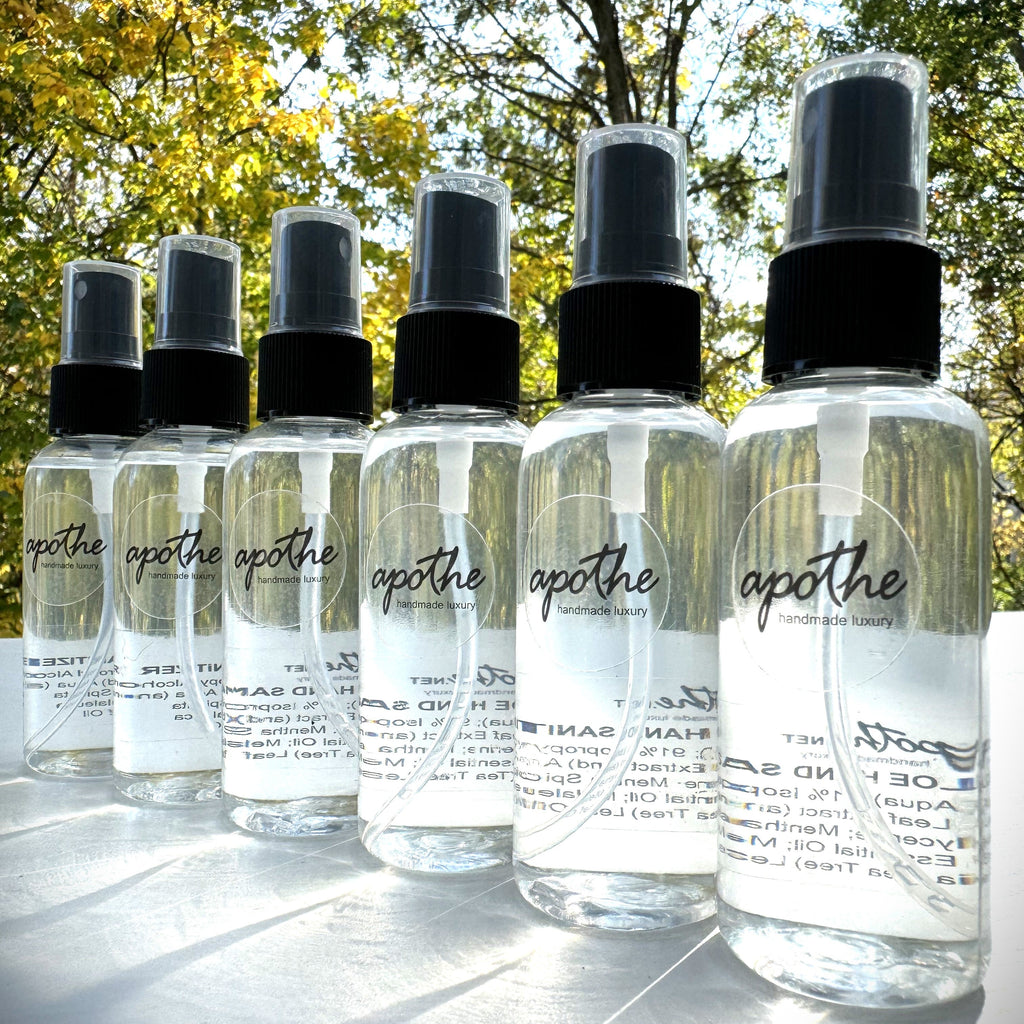Multiple spray bottles of hand sanitizer labeled 'apothe' with a white background, outdoors with trees in the background.