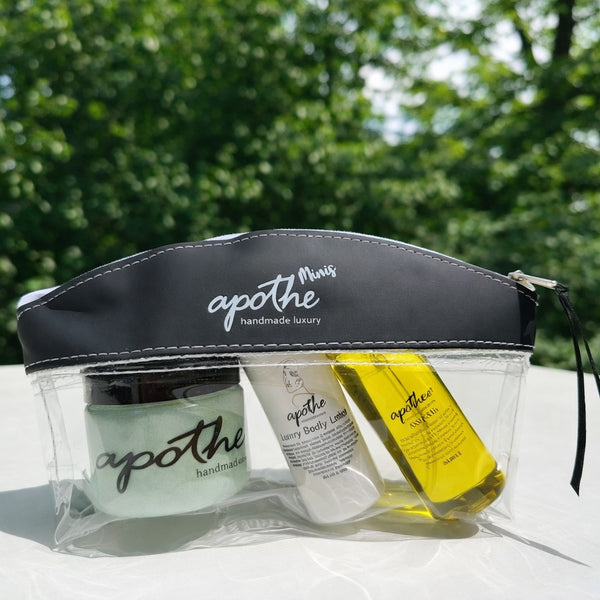  apothe skincare products in a clear pouch with a black top against a green outdoor background featuring skin polish, body lotion and skin oil